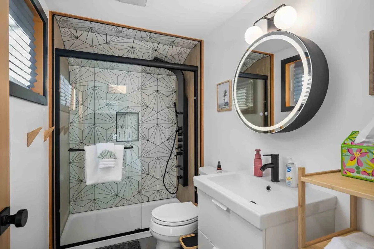 A modern bathroom oasis with a striking geometric-patterned shower wall, circular mirror, and minimalist sink. The inviting design evokes a fresh, spa-like atmosphere perfect for rejuvenation and self-care.