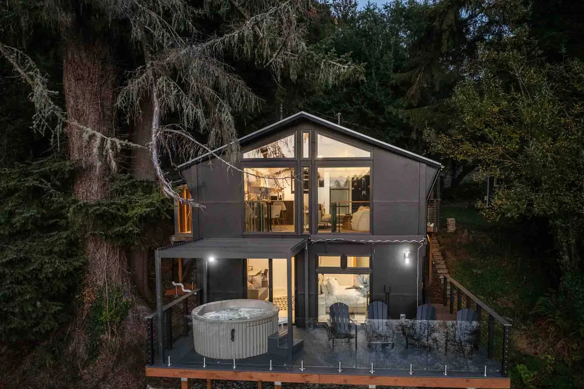 The home's spacious exterior deck features a hot tub surrounded by large windows and nestled among towering trees. The setting is peaceful and inviting—ideal for relaxing after a day of adventure, entertaining guests, or stargazing from the warmth of the tub.