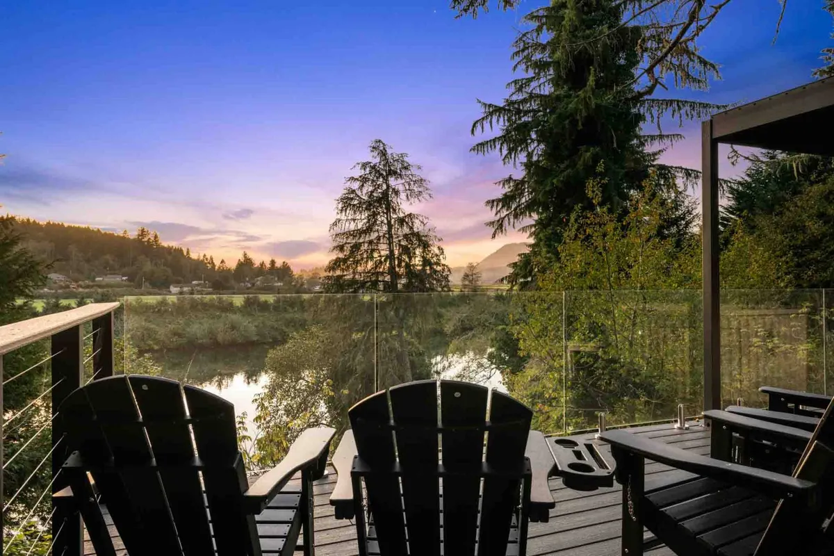 This exterior scene features Adirondack chairs arranged on a deck with a glass railing, set against a backdrop of lush natural landscape. The tranquil, open-air space suggests unwinding at sunset or enjoying quiet moments with a glass of wine while immersed in nature.