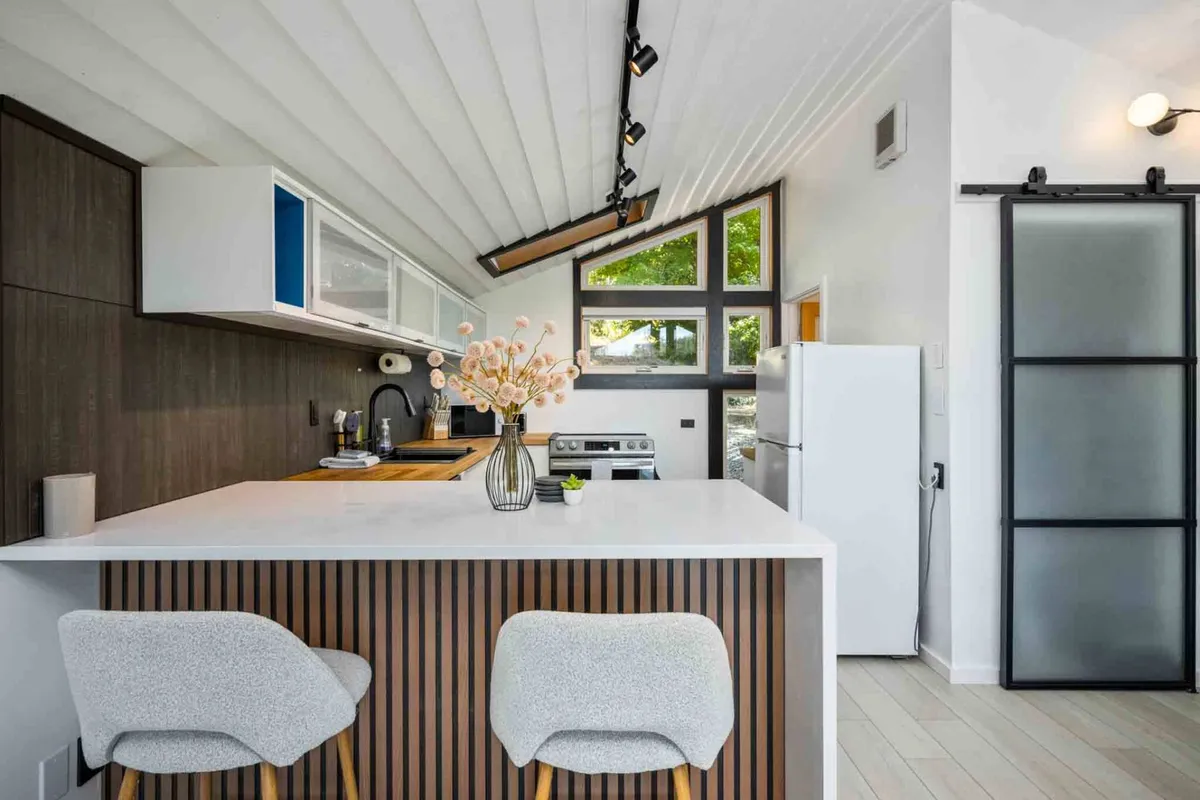 A contemporary kitchen featuring a prominent island, large windows, decorative flowers, and a full suite of modern appliances. The inviting layout encourages both cooking and social gatherings, with the appliances clearly integrated into the cabinetry.