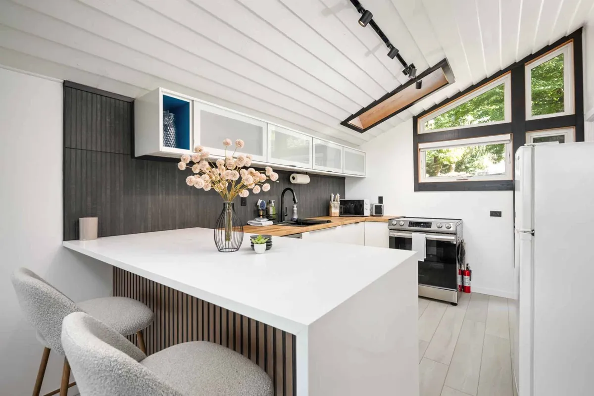 A contemporary kitchen highlighted by a large kitchen island, fresh flowers, and expansive windows. The arrangement invites people to gather, cook together, and enjoy views while preparing meals. Modern fixtures and finishes are evident.