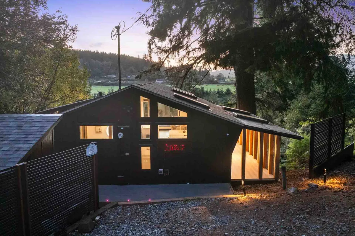 A modern home exterior at dusk, illuminated by warm outdoor lighting. Large windows hint at stylish interiors, while the porch offers inviting vantage points to enjoy the landscape and sunsets.